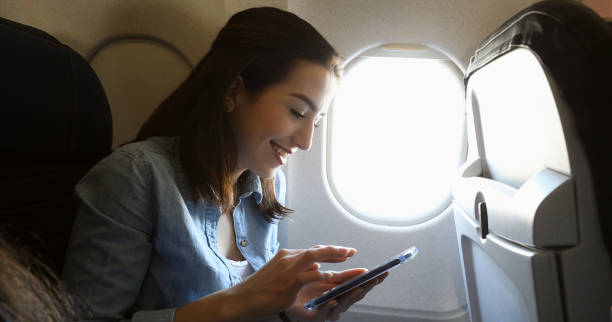 istock Smiling young woman uses phone on airplane 964288680