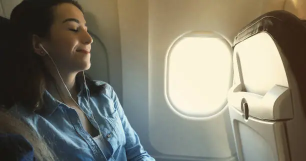 Beautiful young Caucasian woman closes her eyes while listening to music while on a commercial flight.