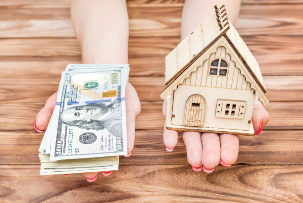Woman's hands holding money and model of house over wooden table. stock photo