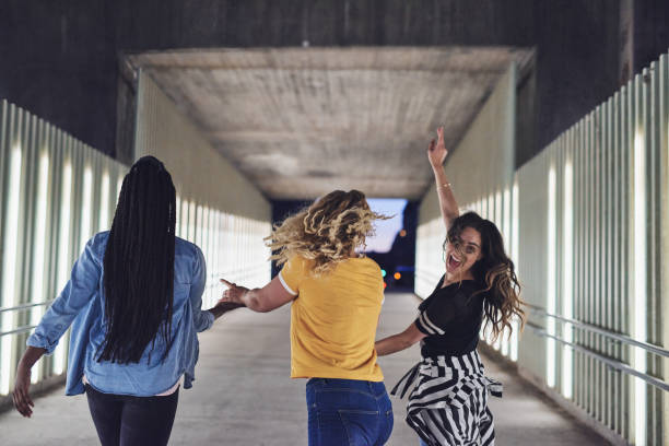 istock Carefree young girlfriends holding hands while walking together at night 964321422