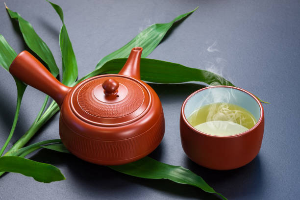 istock Hot tea cup and pot with green leaves on black table 964335062