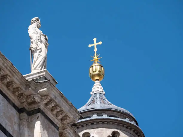 Detail of exterior of Siena Cathedral with scupltute of philosopher and golden cross on cupola