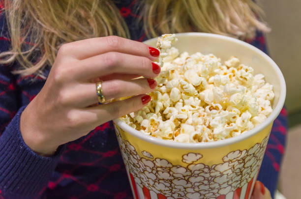 istock Woman's hand close up, picking up popcorn. 964347242