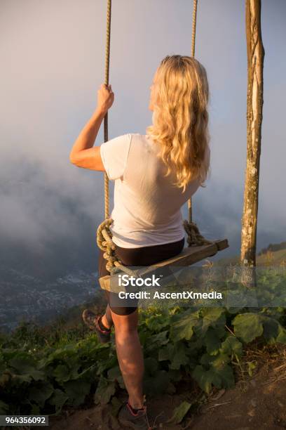 Woman Steps Off Edge To Swing Into Clouds Stock Photo - Download Image Now - Banos, Swinging, Swing - Play Equipment