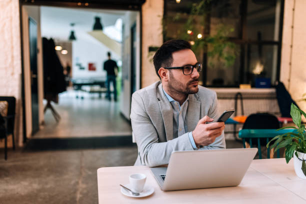 istock Pensive businessman using cellphone while working with laptop. Looking away. 964369108