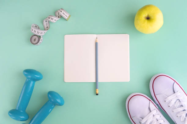 istock White snikers, notebook, dumbbells, green apple and tape measure on mint background 964372734