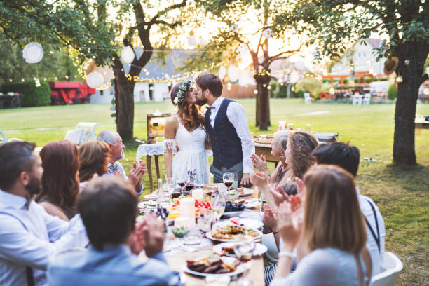 istock Bride and groom with guests at wedding reception outside in the backyard. 964373628