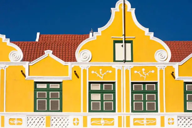 Top part of a colourful classical colonial dutch facade in Curacao, Caribbean island. Tiled roof, ornate facade, wooden windows, yellow wall.