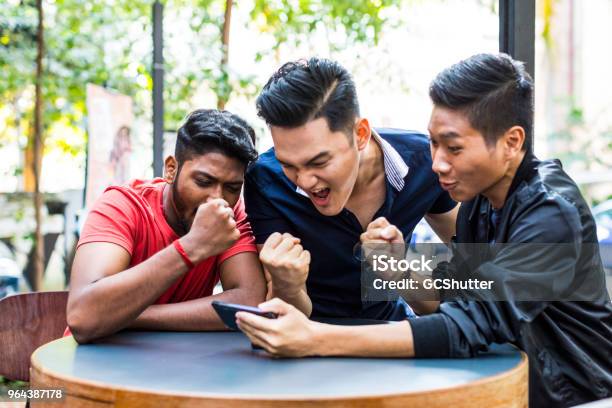 Group Of Friends Watching Their Favorite Match On A Mobile Phone Stock Photo - Download Image Now
