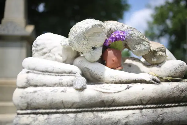 Photo of Stuffed Teddy Bear Lying on Top of a Child's Grave Baby Marble Statue Grave Memorial Marker