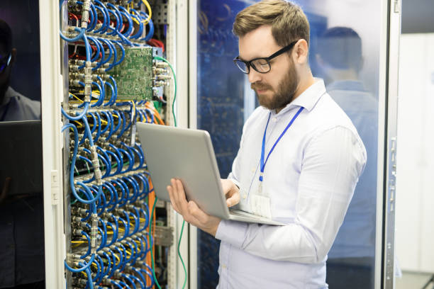 istock Serious concentrated handsome male technician typing on laptop while correcting data taken from supercomputer in server room of mining farm 964442156