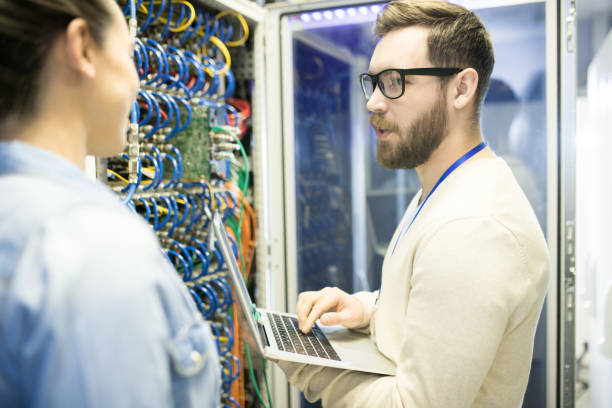 istock Confident highly professional datacenter analyst in glasses examining information on laptop connected to powerful supercomputer and discussing efficiency of this equipment 964442528