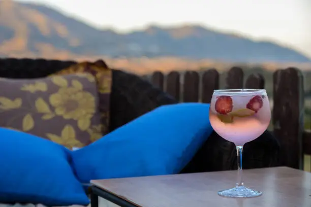 glass with strawberry gin and tonic standing on the table  with mountains and sunset.