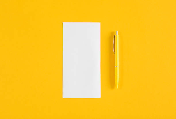 Top view of yellow office desk with white blank and pen.