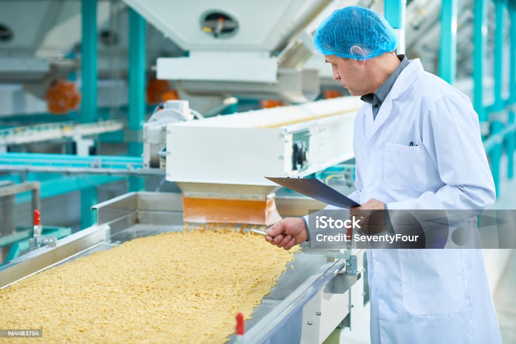 Senior Man at Macaroni Line Side view portrait of senior factory worker doing  production quality inspection in food industry holding clipboard standing by conveyor belt, copy space Food Stock Photo