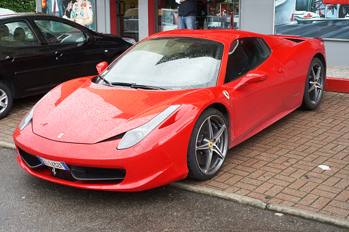 Maranello, Italy - April 27, 2015: Ferrari 458 parked on pavement on a rainy day. Car rental shop in background.