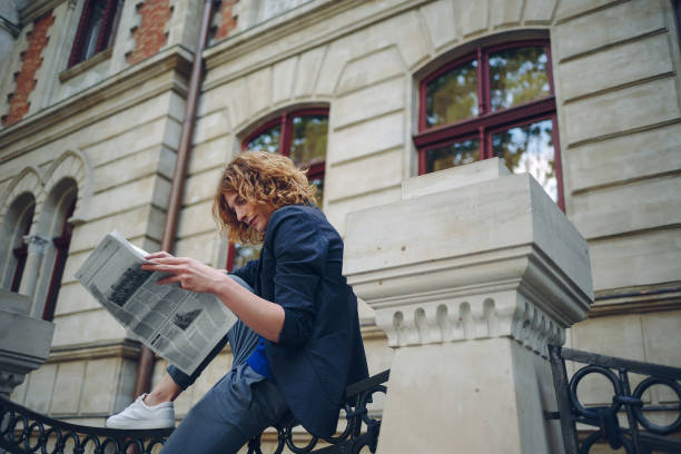 istock Young reddish man reading newspaper near old style building 964487130