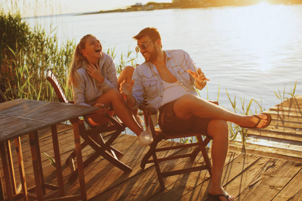 istock Young couple sitting by the river and laughing during the sunset 964487176