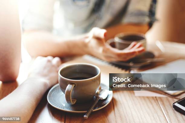 Friends Talking At Cafe Table During Coffee Break Unrecognizable Male And Female Colleagues Discussing Business Issues Focus On Coffee Cup With Saucer And Teaspoon Stock Photo - Download Image Now