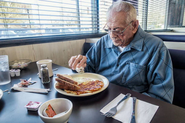 vieil homme adulte senior, saupoudrer de sel de table sur les œufs de petit déjeuner - spice store photos et images de collection