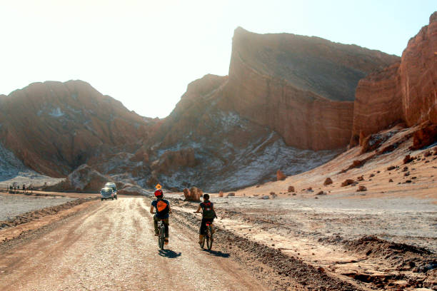 Two adventurous tourists pedal through the Atacama Desert heading for a large rocky wall, stock photo