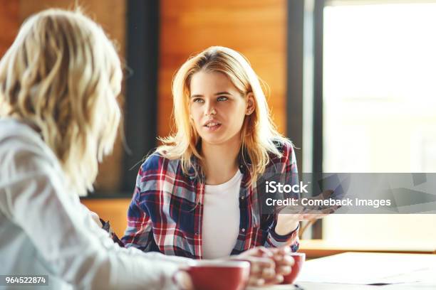 Two Young Female Friends Chatting Over Coffee In Cafe Blonde Women Discussing Issues Stock Photo - Download Image Now