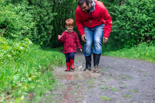 Young Cute Kid Walking Jumping into Water Puddle with Dad Young Cute Kid Walking Jumping into Water Puddle in forest with Dad, Montreal, Canada red boot stock pictures, royalty-free photos & images