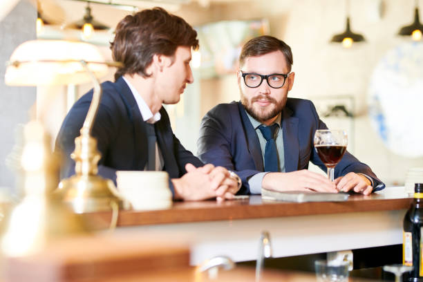 istock Serious confident modern businessmen in suits sitting at bar counter and drinking beer while spending leisure after work 964608486