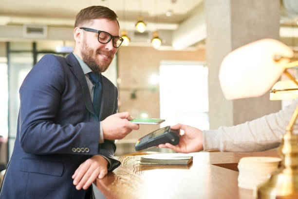 istock Cheerful handsome young businessman in glasses using NFC technology while paying bill through smartphone at bar counter 964608496