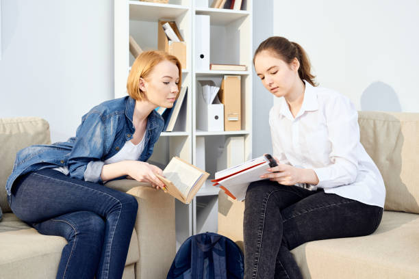 istock Serious brunette girl showing task to groupmate and asking advice while they doing homework together in living room 964629298