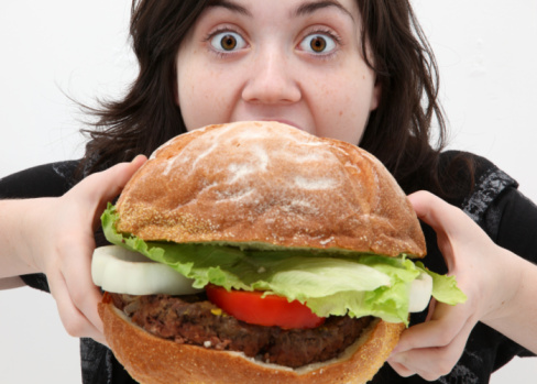 Teenager girl eating a giant hamburger.