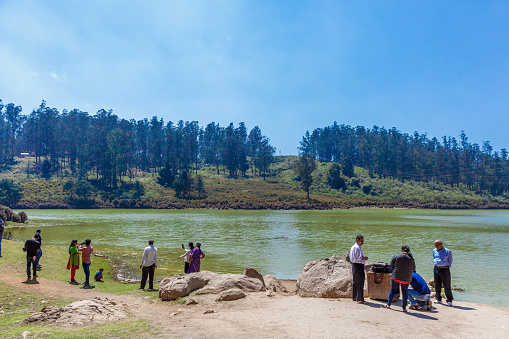 Ooty tamilnadu india August 18 2014 Friends and families spending leisure time near pykara lake surrounded by huge trees in the background