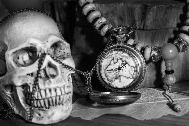 Photo of Still life photography pocket watch , bead necklace and blured human skulls in black adn white