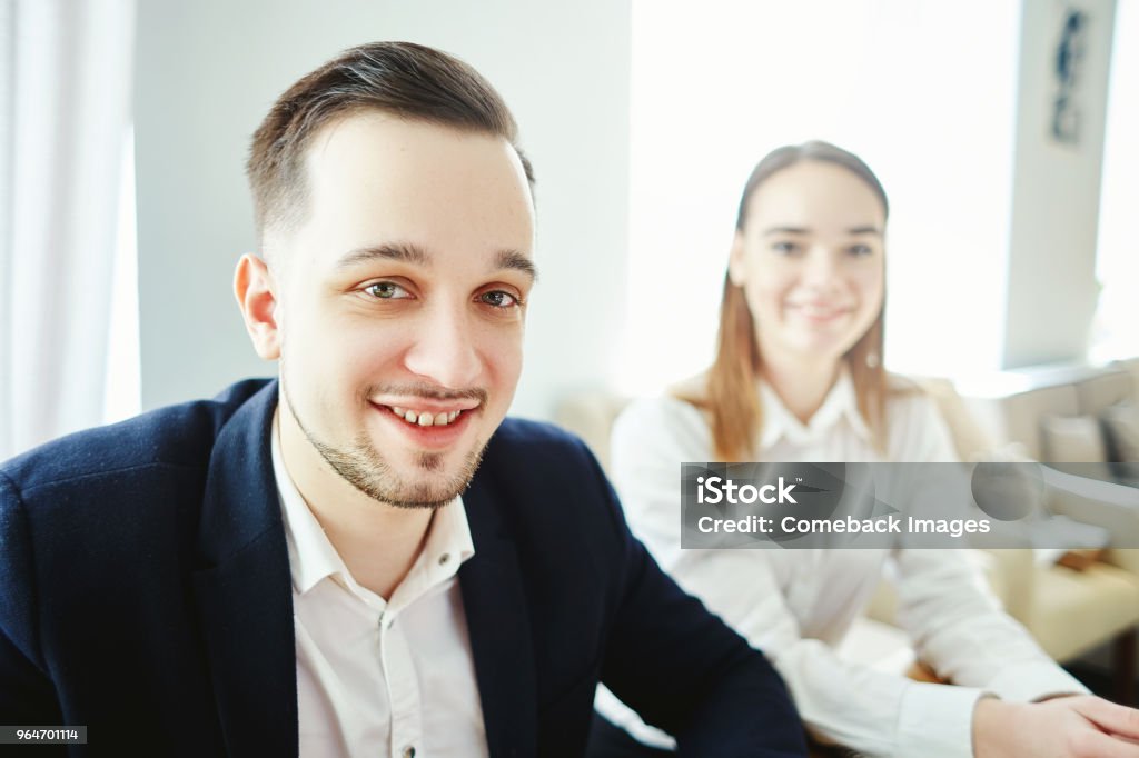 Selfie hymyilevästä nuoresta liikemiehestä, joka katsoo kameraa virallisessa kokouksessa, hänen turmeltunut naiskollegansa taustalla - Rojaltivapaa avainsanalla 2 ja tyyppiä Kuvapankin valokuva