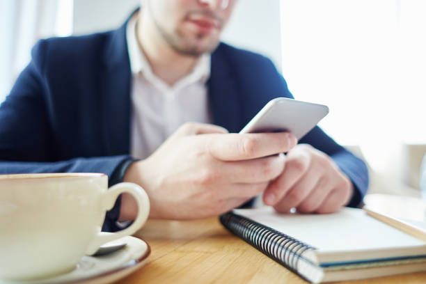 istock Unrecognizable businessman using smartphine while sitting at table in cafe. Coffee cup and open notebook in front of him 964701120
