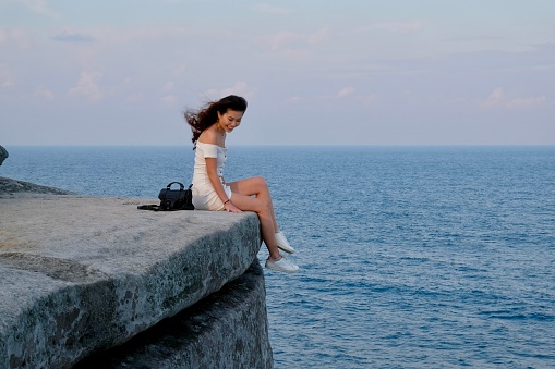 Chinese girl on cliff edge against ocean, afternoon light.