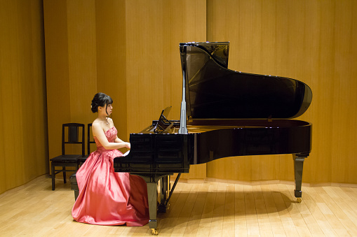 Side view of Japanese woman playing grand piano in a concert, rehearsal.