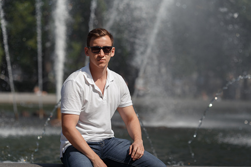 handsome man sitting in sunglasses near fountain. copyspace