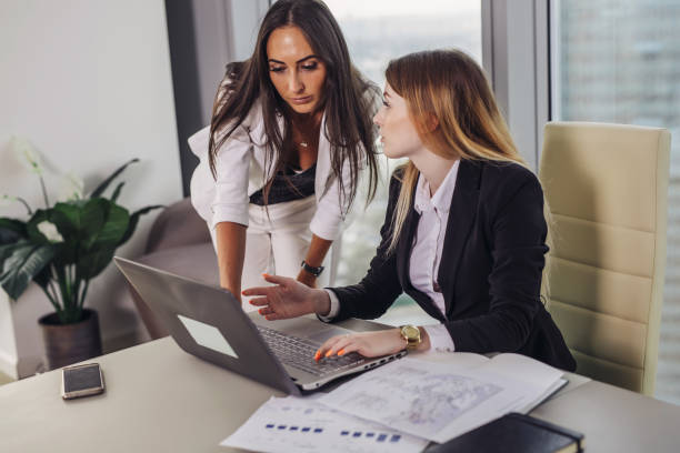 istock Young female assistant consulting with a top manager showing data on laptop screen and asking for advice sitting at working place 964728556