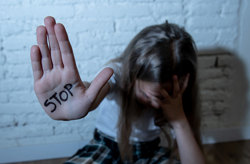 Young cute desperate and scared little schoolgirl showing the text stop bullying written in her hands. Children abused and bullied in school concept. Dramatic light