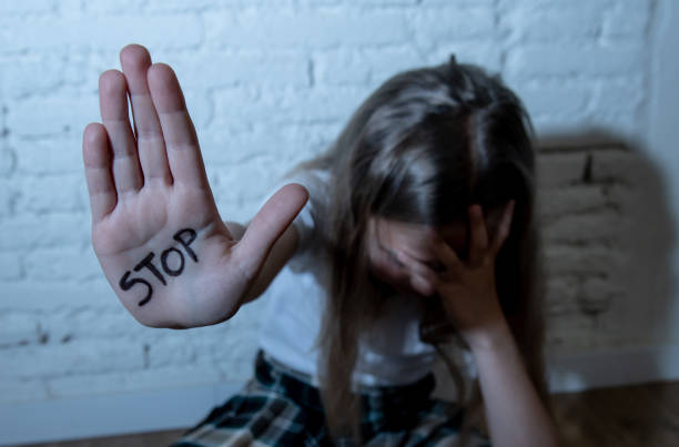 Young cute desperate and scared little schoolgirl showing the text stop bullying written in her hands. Children abused and bullied in school concept. Dramatic light stock photo