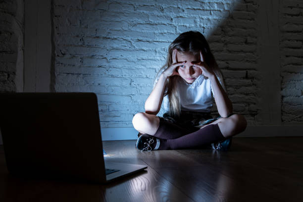 Scared sad girl bullied on line with laptop suffering cyberbullying and harassment feeling desperate and intimidated. Child victim of bullying stalker social media network stock photo