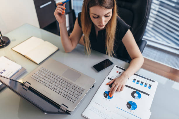 istock Female businesswoman readind financial report analyzing statistics pointing at pie chart working at her desk 964742344