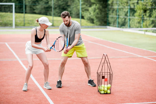 Young woman with male insructor playing tennis Male instructor teaching young woman to play tennis on the tennis court outdoors tennis coach stock pictures, royalty-free photos & images