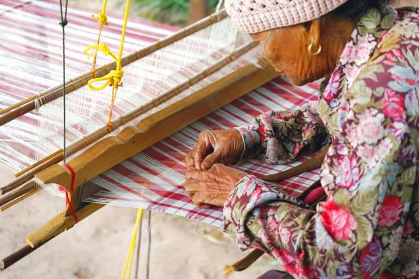 vieille femme thaïlandaise avec ménager traditionnel, tissage machine ou métier à tisser pour tisser la toile de tissage à la main. - tisserin photos et images de collection