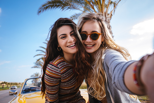 Young hipster girls with convertible car taking selfies on tropical island summer holidays