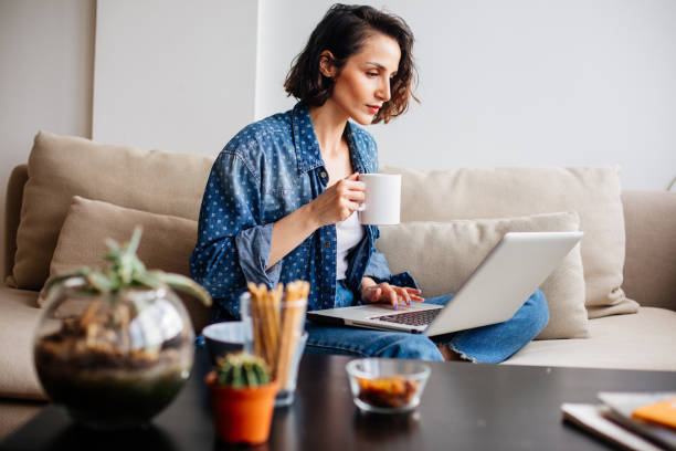 istock Woman using laptop on sofa and drinking coffee 964765674