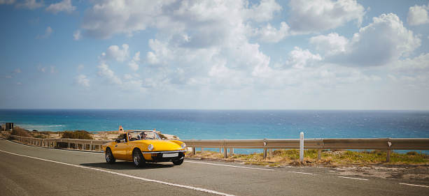 Young hipster women on summer holidays driving yellow vintage convertible car by the sea