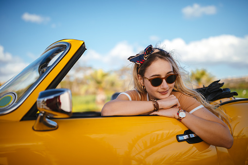 Young hipster woman on road trip summer holidays sitting in vintage convertible car