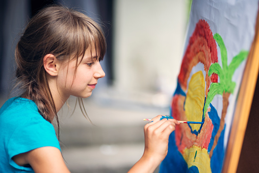 Little girl having fun painting. She is painting on paper and easel. Girl is aged 10.